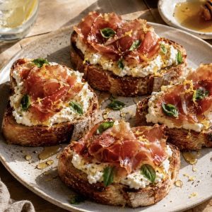 Lemon Ricotta Toast with Crispy Prosciutto & Honey on toasted artisan bread, garnished with herbs and drizzled honey, styled in soft natural light.